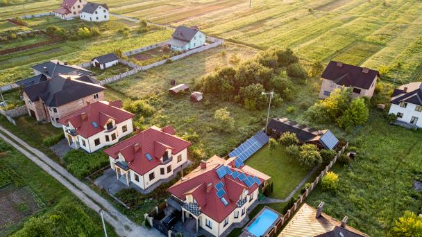 Aerial view of rural residential area with private homes between green fields at sunrise